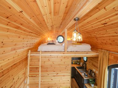 A wooden loft with two beds above a small kitchen area at The Hideaway Pod in Rhoslan near Criccieth