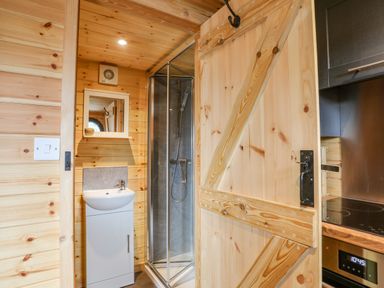 A bathroom with a sink shower and wooden door next to a kitchen area at The Hideaway Pod in Rhoslan near Criccieth