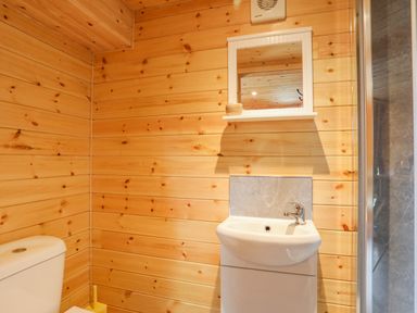 A bathroom with wooden wall panels a white toilet a white sink with a mirror above at The Hideaway Pod in Rhoslan near Criccieth
