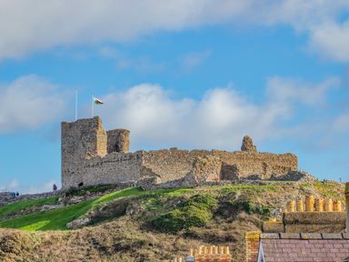 A stone castle on a grassy hill with a flag on top and chimneys of houses in the foreground at The Hideaway Pod in Rhoslan near Criccieth