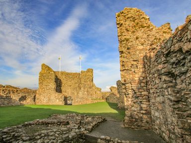 An outdoor view of old stone castle ruins with grassy ground and blue sky