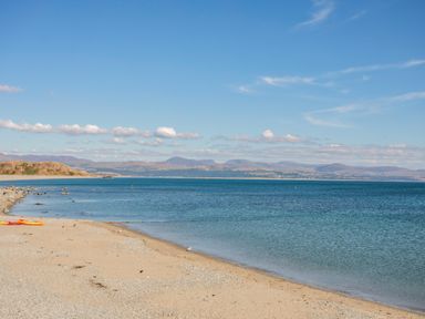 A sandy beach with kayaks near calm sea and mountains in the distance at The Hideaway Pod in Rhoslan near Criccieth