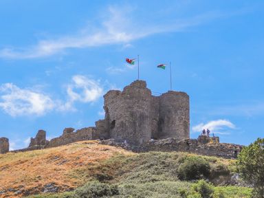 An ancient stone castle on a hill with two Welsh flags flying at The Hideaway Pod in Rhoslan near Criccieth