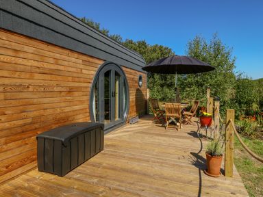 An outdoor wooden deck with a table and chairs under a black umbrella and potted plants at The Hideaway Pod Rhoslan near Criccieth