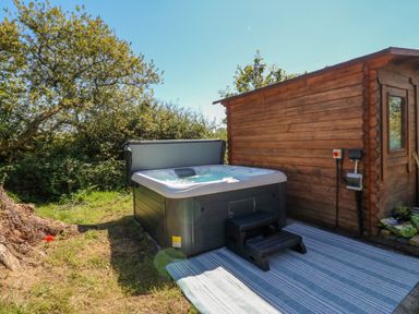 An outdoor hot tub next to a wooden shed with a striped rug on the ground at The Hideaway Pod in Rhoslan near Criccieth