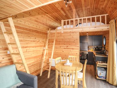 A wooden interior room with a dining table and chairs a kitchen and a loft bed accessed by ladders at The Hideaway Pod in Rhoslan near Criccieth