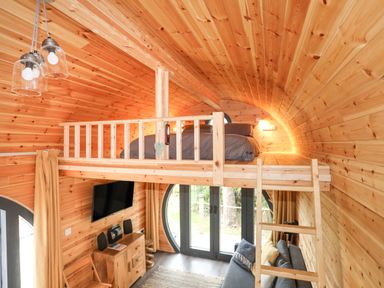 A wooden pod interior with a loft bed dining area sofa and TV at The Hideaway Pod Rhoslan near Criccieth