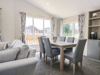 A dining area with a table and six chairs next to large windows and a bookshelf at Parkers Place in Carnforth