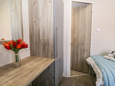 A bedroom with a wooden desk and cabinets a vase with flowers a partially open door and a bed with folded towels at Parkers Place in Carnforth