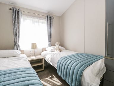 A bedroom with two single beds a nightstand with a lamp between them a window with curtains and a stuffed animal on one bed at Parkers Place in Carnforth