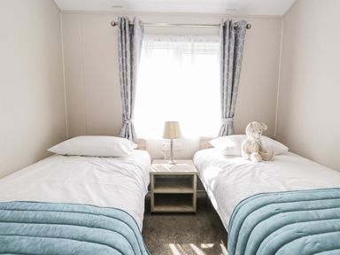 A bedroom with two single beds a bedside table with lamp and window with curtains at Parkers Place in Carnforth