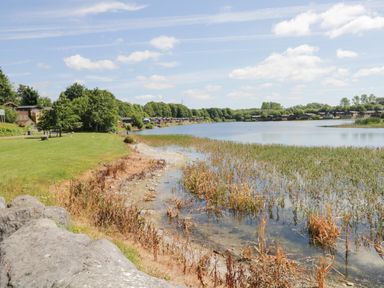 A lakeside with reeds along the shore and multiple small wooden cabins at Parkers Place in Carnforth