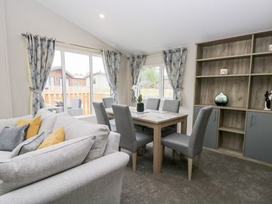 A dining area with a table and six chairs next to a sofa and a shelving unit at Parkers Place in Carnforth