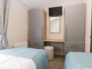 A bedroom with two beds a desk with a round stool a wall-mounted TV and a mirror at Parkers Place in Carnforth