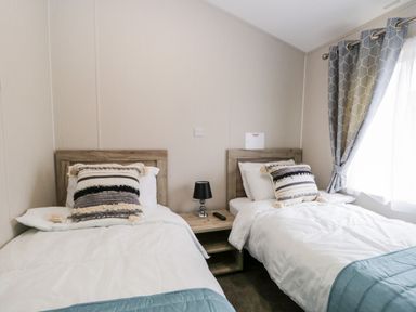 A bedroom with two single beds a wooden nightstand between them a small lamp and a remote control curtains on a window at Parkers Place in Carnforth