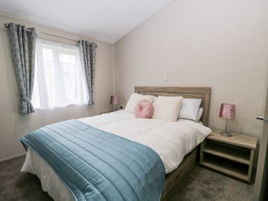 A bedroom with a bed with white and blue bedding flanked by two bedside tables with pink lamps at Parkers Place in Carnforth