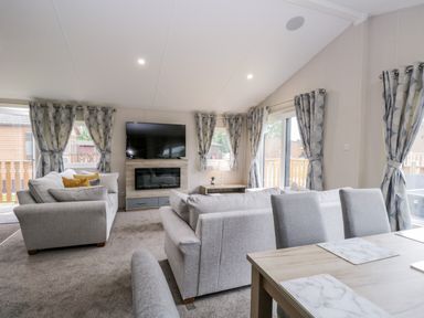 A living room with grey sofas a wall mounted television and windows with curtains at Parkers Place in Carnforth