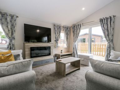 A living room with two sofas a coffee table a television on a stand and curtains at Parkers Place in Carnforth