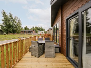 A wooden deck with outdoor furniture next to a building with large windows and sliding door at Parkers Place in Carnforth