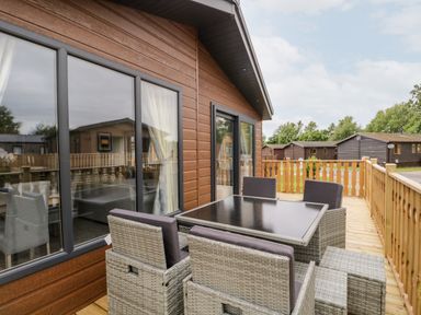 An outdoor patio with a wicker dining table and six chairs on a wooden deck at Parkers Place in Carnforth