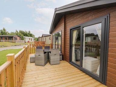 A wooden deck with outdoor dining furniture attached to a cabin with sliding glass doors at Parkers Place in Carnforth