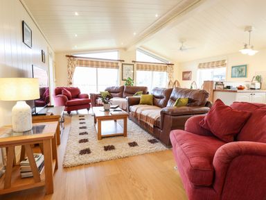 A living room with red and brown sofas a wooden coffee table a patterned rug and large windows at Tanqueray Lodge in Kenwick near Louth