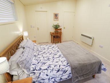 A bedroom with a wooden bed with patterned bedding a small wooden desk with a chair and flowers between two doors at Tanqueray Lodge Kenwick near Louth