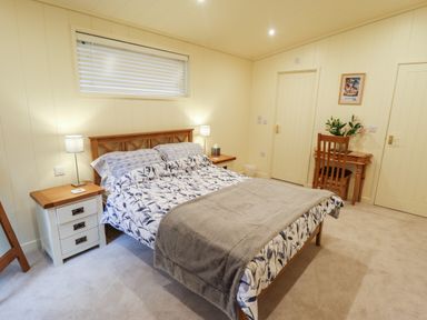 A bedroom with a double bed bedside tables with lamps a wooden desk with a chair and flowers at Tanqueray Lodge Kenwick near Louth