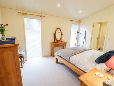 A bedroom with a wooden bed, dresser, dressing table, clothes rack, and two windows at Tanqueray Lodge Kenwick near Louth