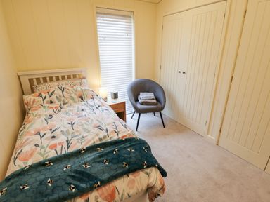 A bedroom with a single bed floral bedding a bedside table with a lamp a gray chair with folded towels and a built in wardrobe at Tanqueray Lodge Kenwick near Louth