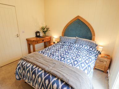 A bedroom with a bed with blue patterned bedding bedside tables lamps a wooden desk a vase with flowers and a door at Tanqueray Lodge in Kenwick near Louth