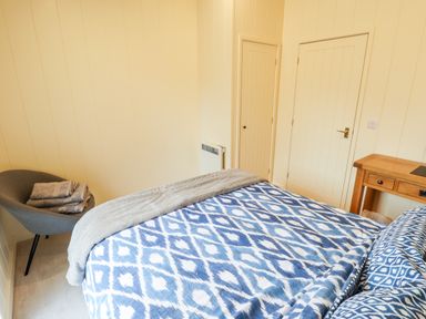 A bedroom with a bed covered in blue and white patterned bedding a grey chair with folded towels and a wooden desk at Tanqueray Lodge in Kenwick near Louth