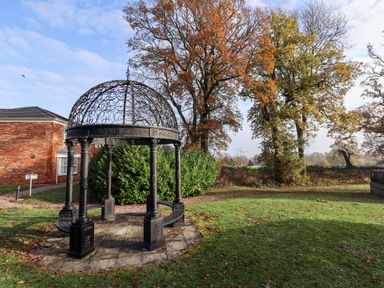 A metal gazebo structure on a paved area with grass and trees in the background at Tanqueray Lodge in Kenwick near Louth