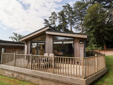 A wooden cabin with a fenced deck and outdoor table and chairs surrounded by trees at Tanqueray Lodge in Kenwick near Louth