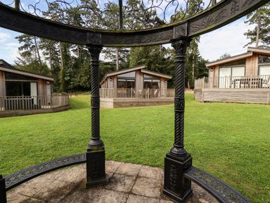 Three wooden lodges with balconies on a grassy area viewed through black decorative metal columns at Tanqueray Lodge Kenwick near Louth