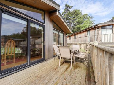 An outdoor wooden deck with a glass table and four chairs outside wooden lodges at Tanqueray Lodge Kenwick near Louth
