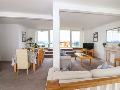 A living and dining area with beige sofas a wooden dining table and chairs a coffee table and a fireplace at Apartment at Morningside Hotel in Torquay