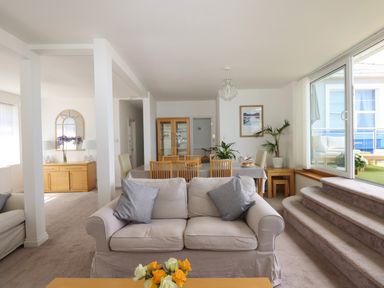 A living room with sofas a dining table with chairs and plants near large windows at Apartment at Morningside Hotel in Torquay