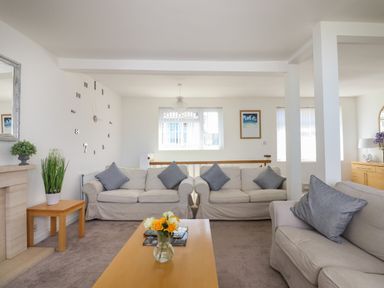 A living room with three sofas a wooden coffee table with flowers a decorative wall clock and a window at Apartment at Morningside Hotel in Torquay