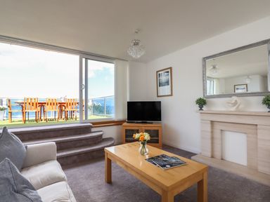 A living room with a sofa coffee table and television next to sliding glass doors leading to a balcony at Apartment at Morningside Hotel in Torquay