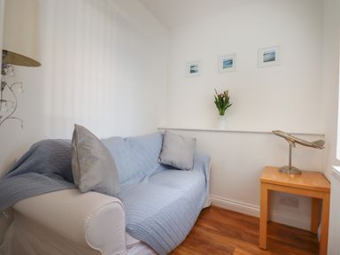A small sitting area with a white sofa covered with a blue throw and two grey cushions a wooden side table with a metal airplane model and three small framed pictures on the wall at Apartment at Morningside Hotel in Torquay
