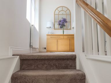 A staircase with carpeted steps leading to a wooden sideboard with a mirror a lamp and flowers at Apartment at Morningside Hotel in Torquay