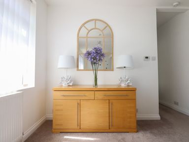A wooden sideboard with two white lamps and a vase of purple flowers under an arched mirror in a room at Apartment at Morningside Hotel in Torquay