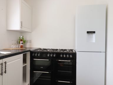 A kitchen corner with a black double oven stove and a white refrigerator with water dispenser at Apartment at Morningside Hotel in Torquay