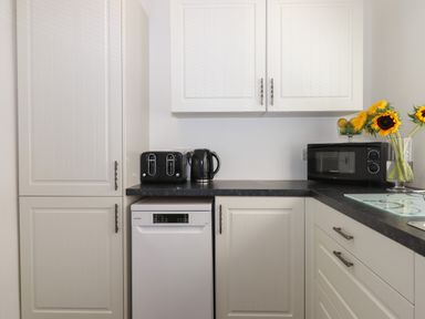 A kitchen corner with white cabinets black countertop a toaster electric kettle microwave and sunflowers in a vase at Apartment at Morningside Hotel in Torquay