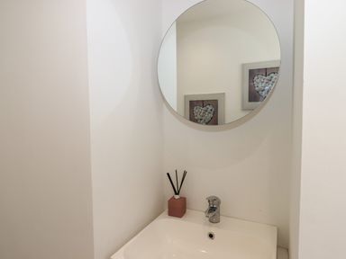 A bathroom sink with a faucet a round mirror and a diffuser at Apartment at Morningside Hotel in Torquay