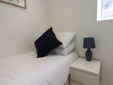 A single bed with white linens a black pillow and a bedside table with a black lamp at Apartment at Morningside Hotel in Torquay