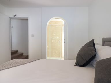 A bedroom with a bed featuring grey pillows and a view into a bathroom through an arched doorway at Apartment at Morningside Hotel in Torquay