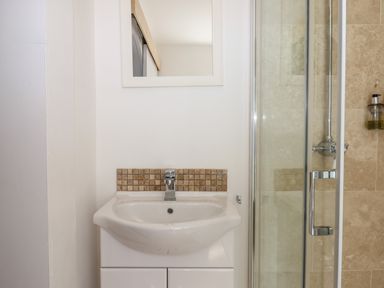 A bathroom sink with a faucet and a mirror above next to a glass shower door at Apartment at Morningside Hotel in Torquay