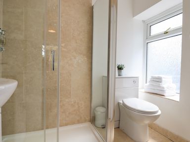 A bathroom with a shower enclosure a toilet a stack of towels on the window ledge and a small plant at Apartment at Morningside Hotel in Torquay